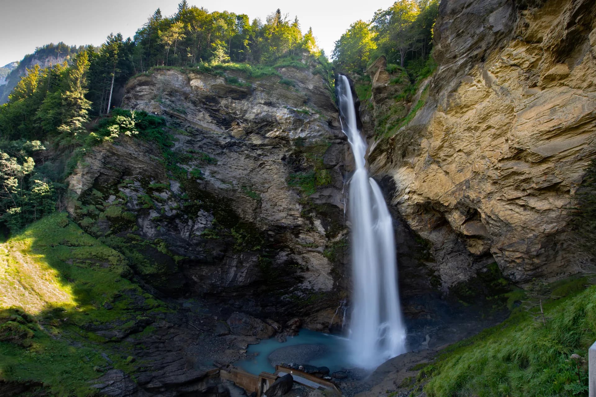 Tall waterfall plunging down rocky cliffs surrounded by green forest in Switzerland.