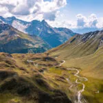 Aerial view towards the Capanna Motterascio, an alpine hut on the Greina plateau in Blenio, Swiss Alps. A rocky ridge on the right leads the eye towards the river that flows sinuously in the hilly